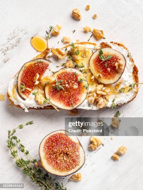 sandwiches mit frischen feigen, käse, thymian und honig an bord. feigenbruschetta, brot und frischkäse und obst auf weißem hintergrund. sandwiches mit ricotta, frischen feigen, walnüssen und honig auf weißem hintergrund. bruschetta mit feigen, käse, - blauschimmelkäse stock-fotos und bilder