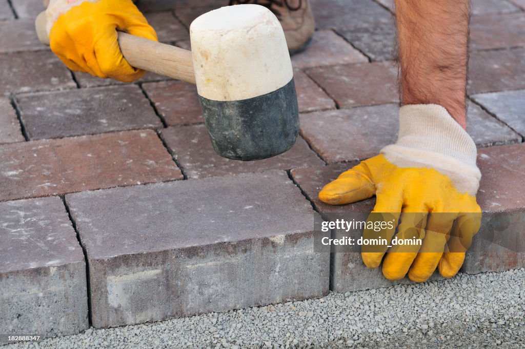 Pedreiro organiza cobblestones, close-up, as mãos em luvas de protecção, Macete de Borracha