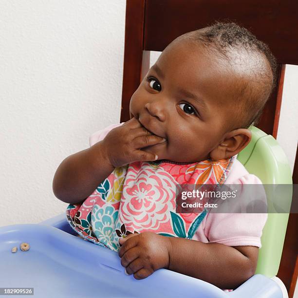 african descent baby girl eating cheerios, bib, high chair - eating with a bib stock pictures, royalty-free photos & images