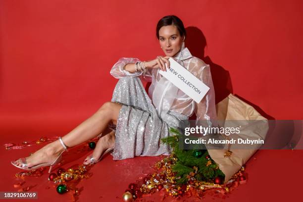 beautiful young fashionable woman sitting on a red background posing in a new collection of christmas clothes. christmas sale concept. - glamour fotografías e imágenes de stock