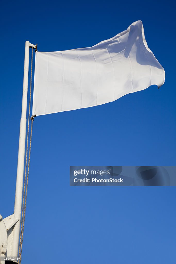 Empty white flag waves in front of deep blue sky