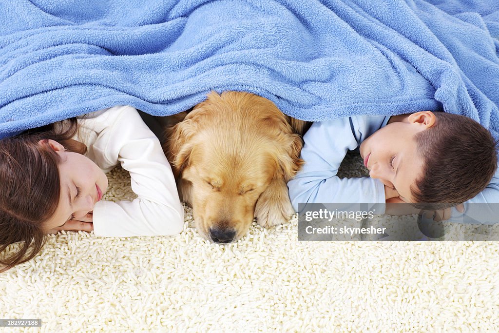 Boy, girl and dog sleeping covered with a blanket.