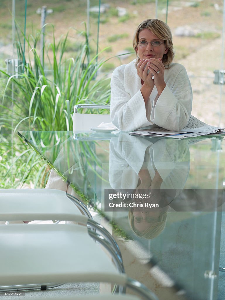 Frau im Bademantel in Glas Zimmer mit Kaffee lächelnd