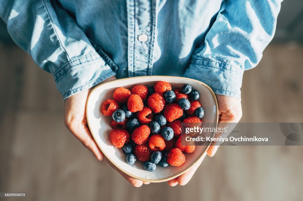 A woman holds a plate of fruits and berries in her hands