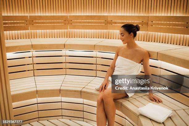 young woman relaxing and sweating in hot sauna wrapped in towel. - cipresso stock-fotos und bilder