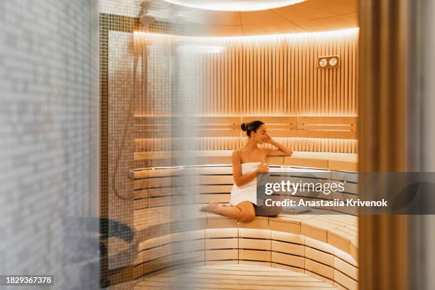 young woman relaxing and sweating in hot sauna wrapped in towel. - cipresso stock-fotos und bilder