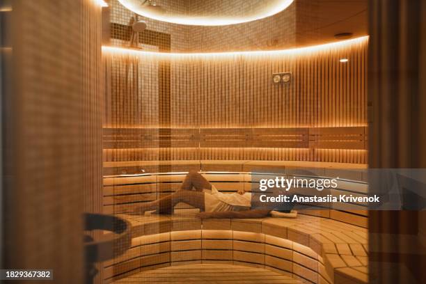 young woman relaxing and sweating in hot sauna wrapped in towel. - health spa stock pictures, royalty-free photos & images