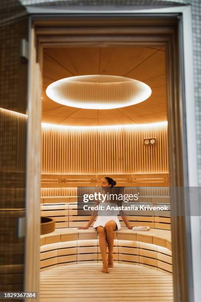 young woman relaxing and sweating in hot sauna wrapped in towel. - health spa stock pictures, royalty-free photos & images