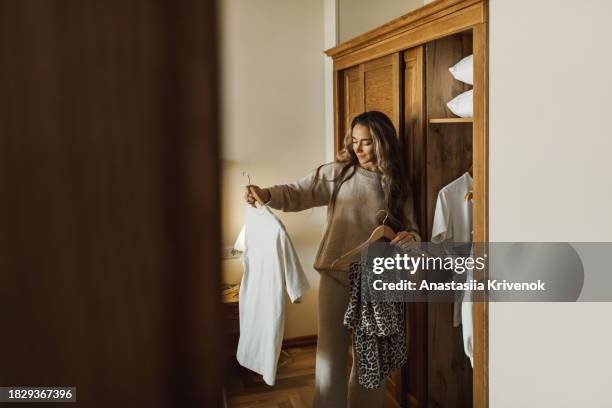 cute young woman selecting clothes from her wardrobe for work or walk. - vestirse fotografías e imágenes de stock