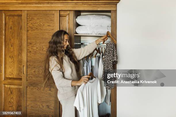 cute young woman selecting clothes from her wardrobe for work or walk. - cipresso stock-fotos und bilder