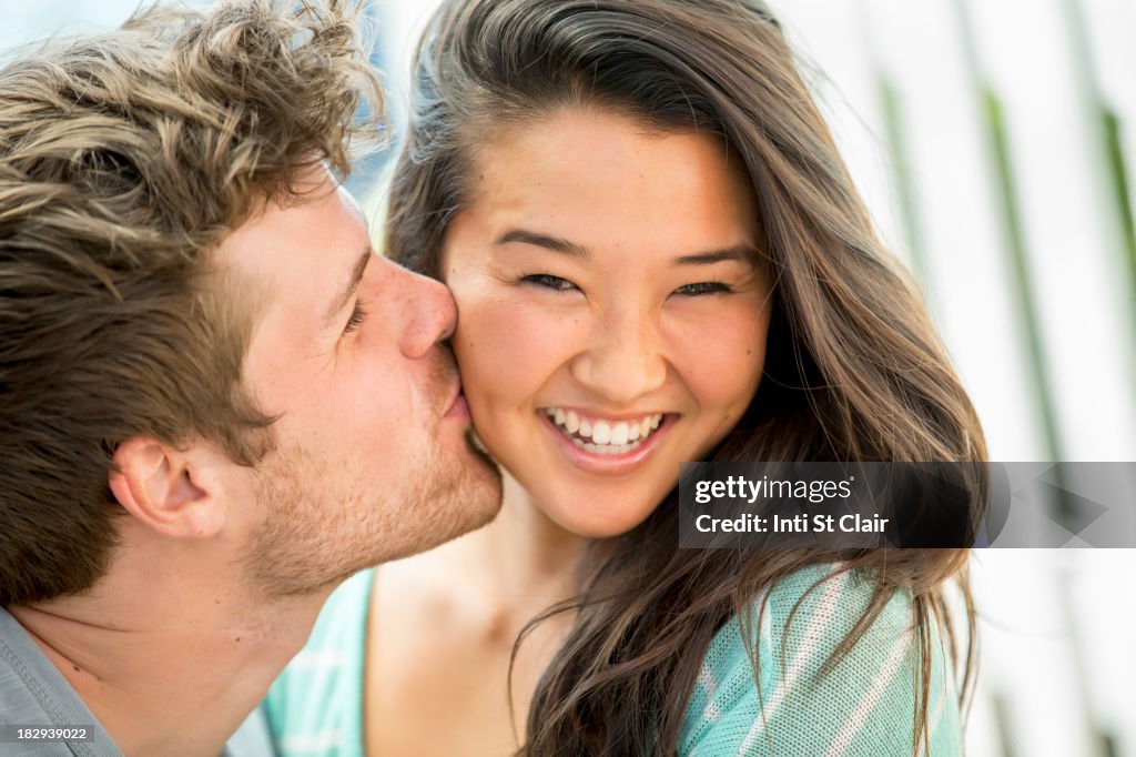 Man kissing girlfriend's cheek outdoors