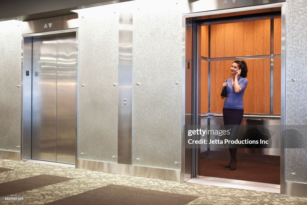 Mixed race businesswoman on cell phone in elevator