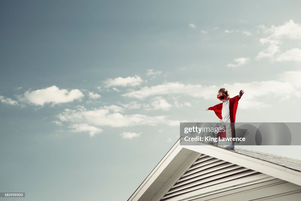 Caucasian boy in cape at edge of roof