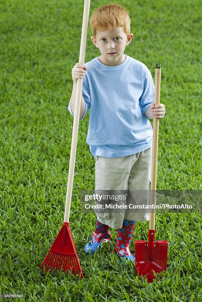 Boy holding rake and shovel, full length portrait
