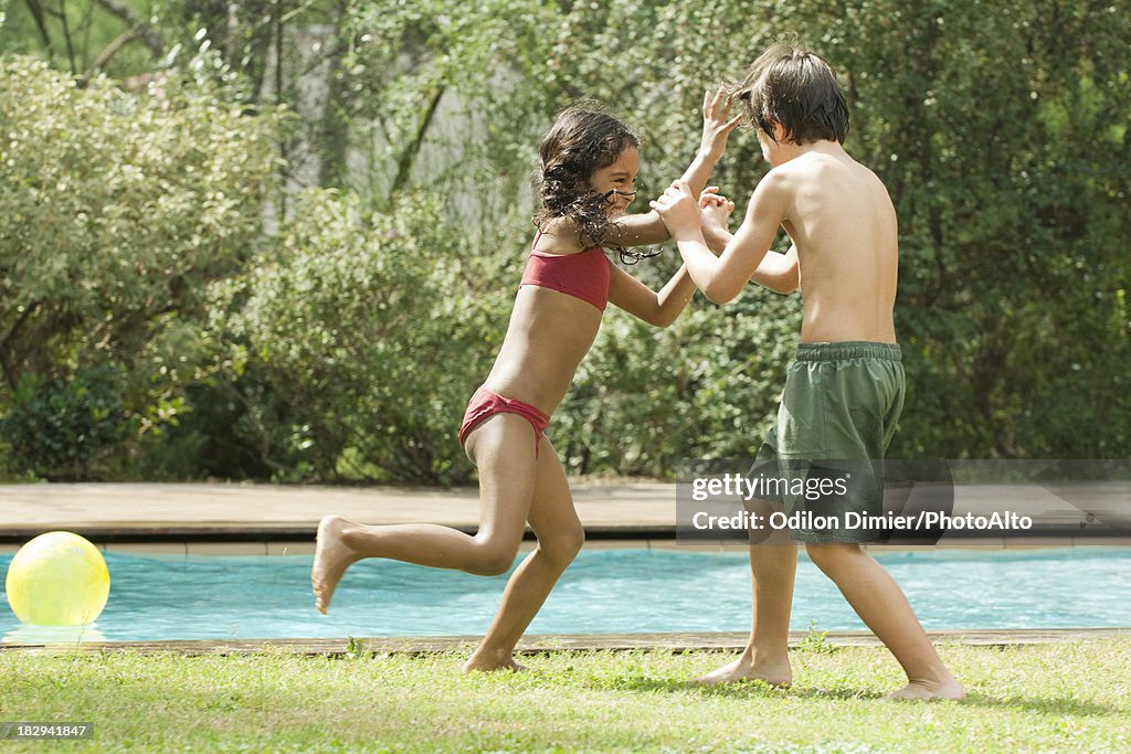 Boy and girl playfighting at poolside