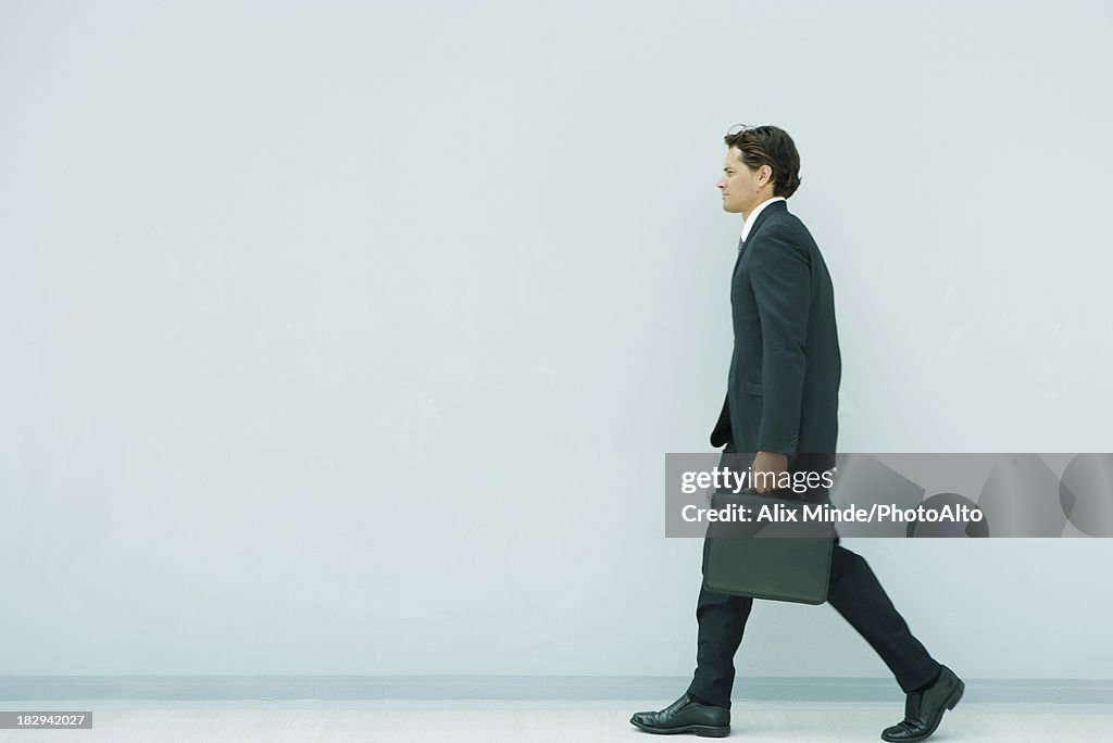 Young executive walking briefcase, side view