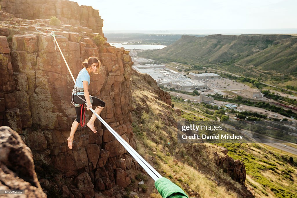 Girl sitting on a high slack line over a town.