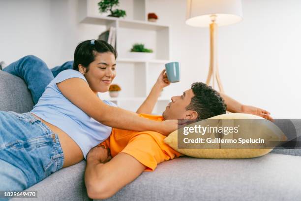 couple cuddling and drinking coffee on the sofa - tiener koppel stockfoto's en -beelden