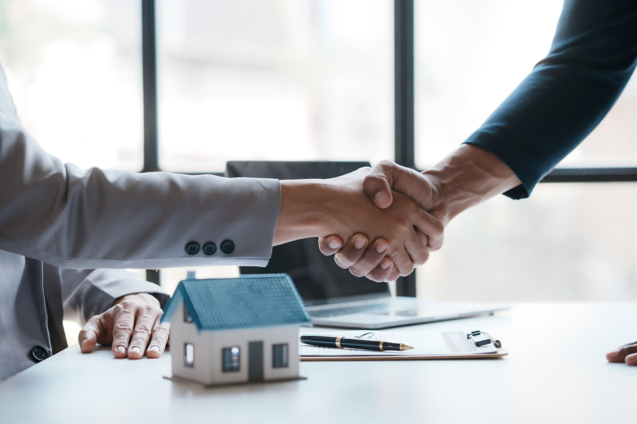 Real estate agent shakes hands with a client to sign a home purchase contract congratulating the client on the purchase. Real estate agent shakes hands with a client to sign a home purchase contract congratulating the client on the purchase.