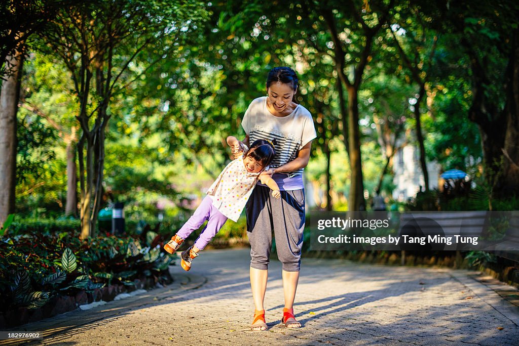 Young mom swinging toddler girl in a park joyfully