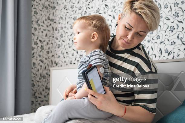 kontrolle von diabetikern. mutter überprüft den blutzuckerspiegel ihres sohnes mit einem fernsensor. überwachung des blutzuckerspiegels ohne blut. medizintechnik in der diabetes-behandlung. - fühler stock-fotos und bilder