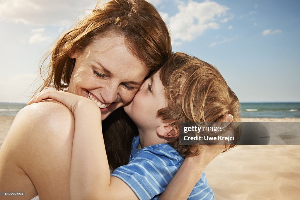 Boy (4-5 years) kissing mother, smiling, close up