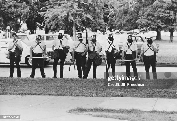 Police officers wearing gas masks and carrying nightsticks watch the protestors from a distance on the Poor People's Campaign, an organised...