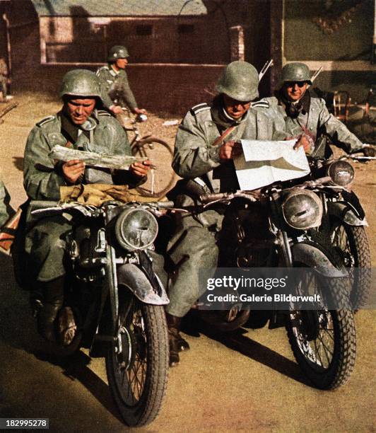 Three German soldiers of the Wehrmacht on motorcycles are studying road maps, France, circa 1940. One is on a bicycle. Motorcycle units were...