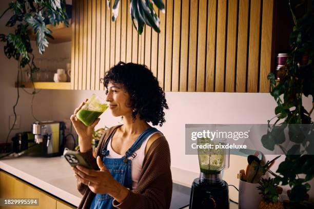 a young nutritionist at home drinking a nutritious smoothie with fresh produce to enhance metabolism and vitamin intake, planning her weekly meals on her smartphone - smoothie bildbanksfoton och bilder