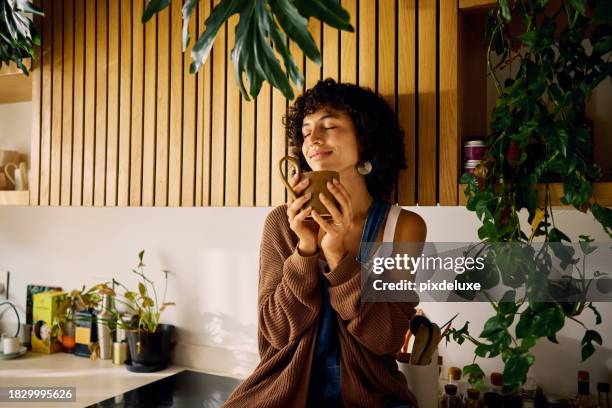 mujer contenta saboreando el aroma de su café de la mañana en una cocina bien iluminada con acentos modernos de madera y exuberantes plantas de interior, abrazando un momento de serenidad, simbolizando la atención plena y la alegría de los placeres sim - chica-tomando-cafe fotografías e imágenes de stock