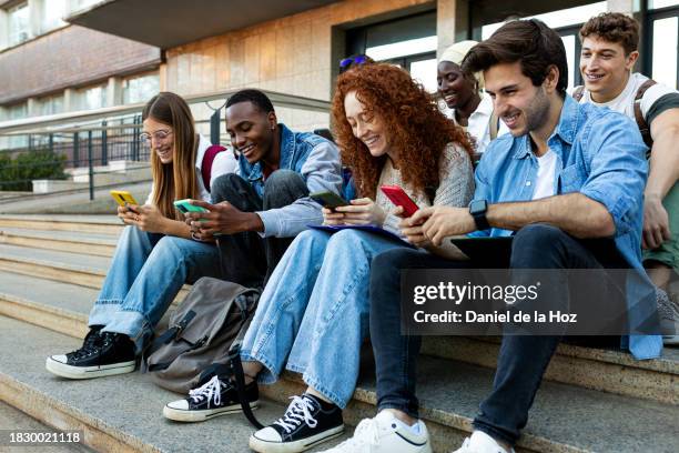 group of happy young college student friends look at mobile phone laughing together. multiracial teenagers using smartphone outdoor university building. - college application stockfoto's en -beelden