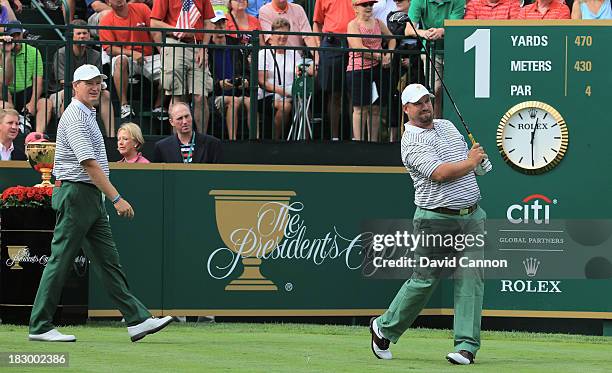 Brendon de Jonge of Zimbabwe and the International Team hits his tee shot on the first hole as Ernie Els looks on during Day One Four-Ball Matches at...