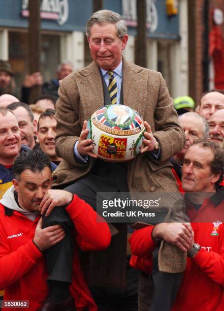 Britain's Prince Charles holds a ceremonial ball as he is carried by participants of the ancient Royal Shrovetide Football game March 5, 2003 in...