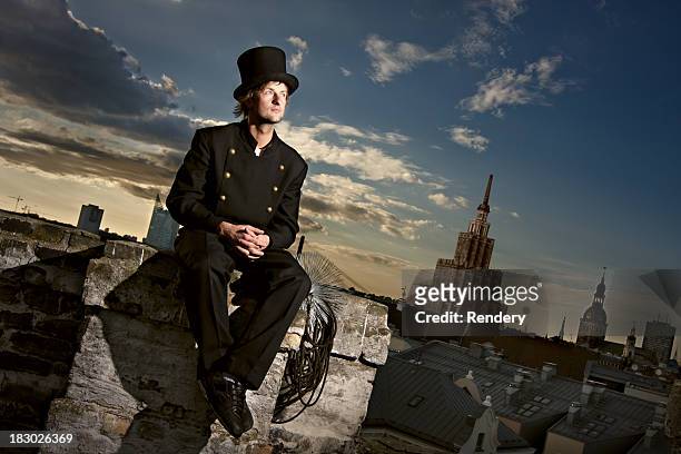 chimney sweep sitting on the roof with city in background - 掃地 個照片及圖片檔