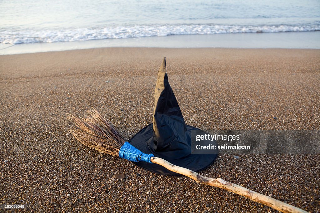 Witch's Hat And Broom On Beach Sand By Sea Vawes