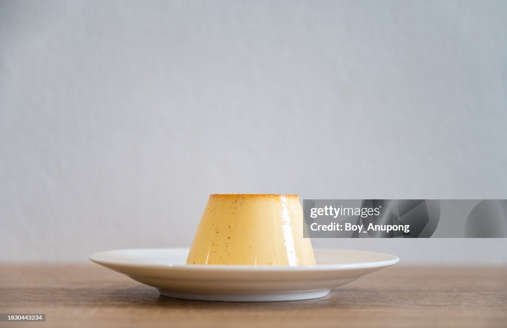 A sweet pudding served in a plate on table against the white wall.