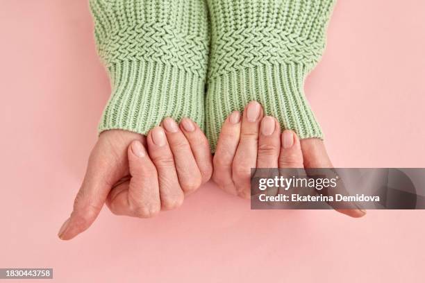female adult hands with fingers manicured nude nails holding knitted sweater sleeves on pink studio background - fingernagel stock-fotos und bilder