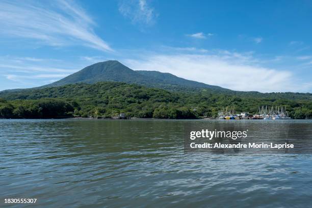 coastline seen from afar with a volcanic mountain, lush vegetation forest and a small marina with boats with a calm ocean - salvadorianische kultur stock-fotos und bilder