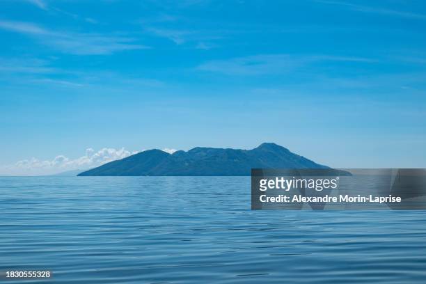 island seen from afar with volcanic hills, lush vegetation forest in front of a calm ocean - salvadorianische kultur stock-fotos und bilder