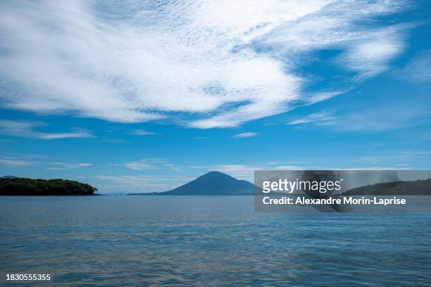 beautiful volcanic island seen from afar between two other islands with volcanic hills, patches for grazing and forest in front of a calm ocean with birds and boats - salvadorianische kultur stock-fotos und bilder