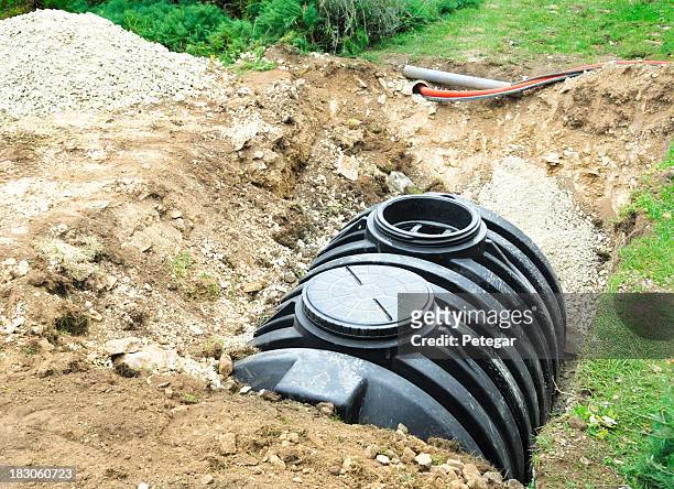 a black septic tank halfway buried in dirt outside - sewage stockfoto's en -beelden