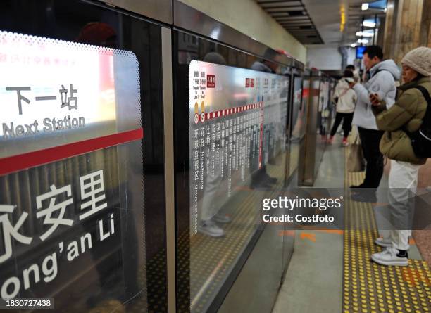 Passengers wait under a bilingual sign at Jianguomen subway station in Beijing, China, December 7, 2023. Signs in both Chinese and English have been...