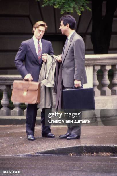 American actor Willem Defoe and American actor Joe Mantegna, both dressed in suits, carrying briefcases and carrying their coats over their arms,...