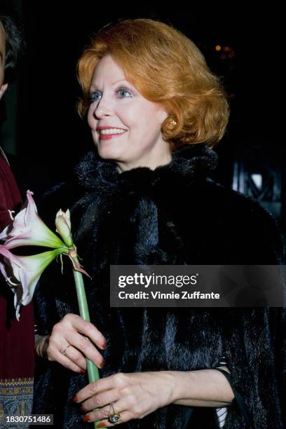 American actress Arlene Dahl wearing a black fur coat, holds a lily flower, United States, circa 1995.