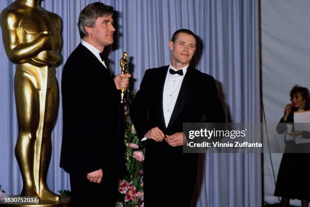 British production designer Stuart Craig, holding his Best Art Direction award, alongside American actor Willem Dafoe, with his head shaved, in the...