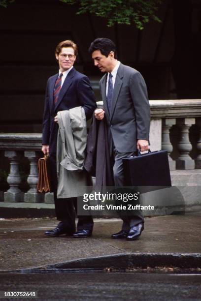 American actor Willem Defoe and American actor Joe Mantegna, both dressed in suits, carrying briefcases and carrying their coats over their arms,...