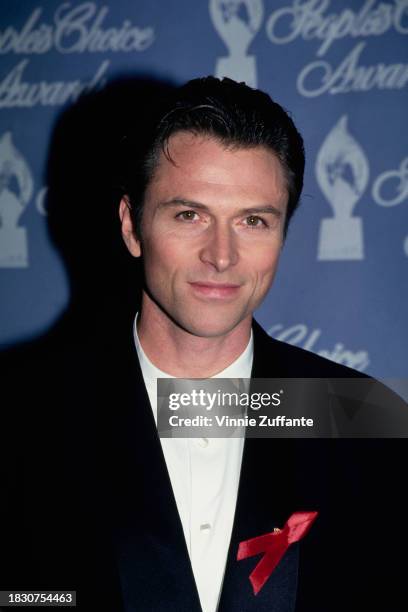 American actor Tim Daly, wearing a black jacket over a white collarless shirt, with an AIDS awareness ribbon, attends the 21st Annual People's Choice...