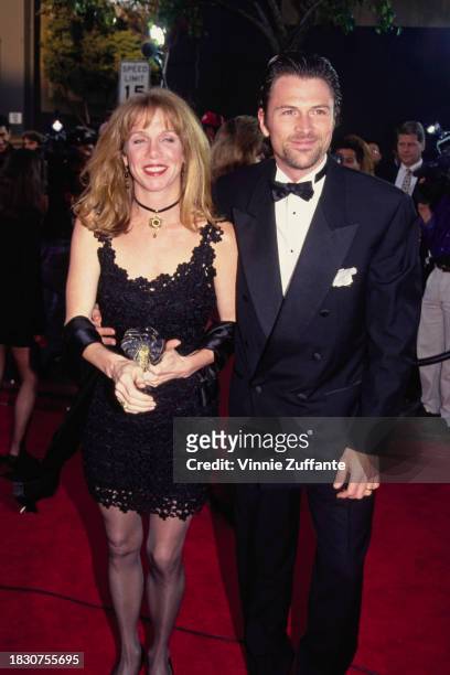American actress Amy Van Nostrand, wearing a black dress with black lace trim, and her husband, American actor Tim Daly, who wears a tuxedo and bow...