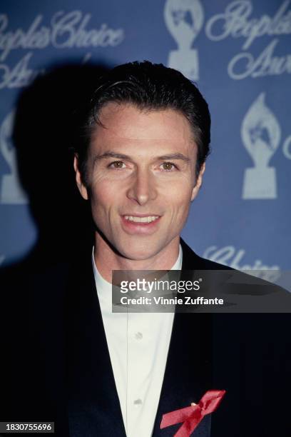 American actor Tim Daly, wearing a black jacket over a white collarless shirt, with an AIDS awareness ribbon, attends the 21st Annual People's Choice...