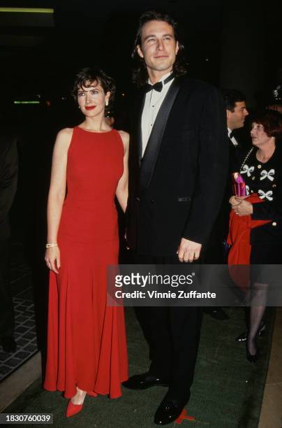 American actress Janine Turner, wearing a red sleeveless full-length dress, with American actor John Corbett, who wears a tuxedo and bow tie, attend...
